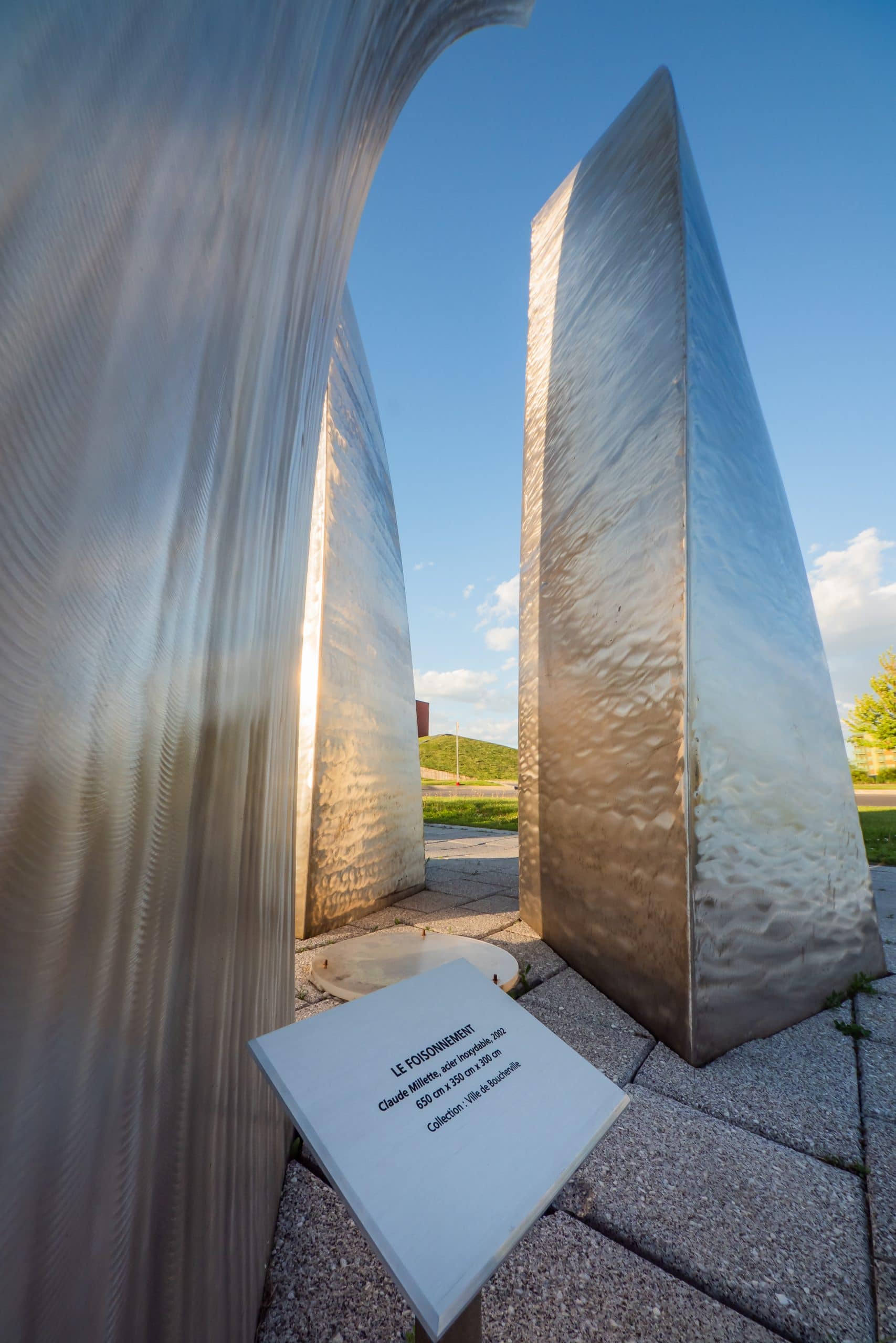 Catalogue d'art public - Claude Millette : Le Foisonnement - Sculpture de trois grandes colonnes métalliques courbées évoquant des éléments organiques en mouvement.