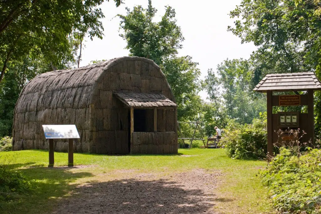 Une maison ancestrale faite de bois et de paille, située dans un espace gazonné et entouré de végétation.  