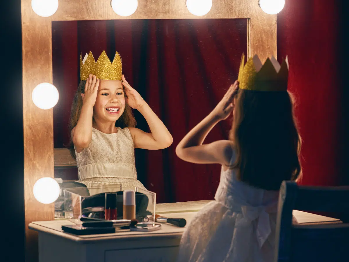 petite fille portant une couronne devant une miroir au théâtre
