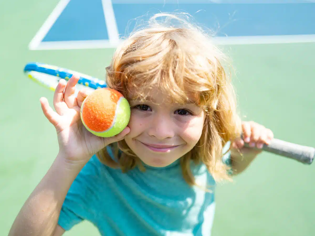 Un enfant tient une balle de tennis et une raquette.